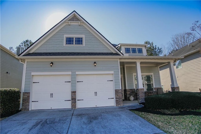 craftsman-style home featuring a garage, concrete driveway, covered porch, and stone siding