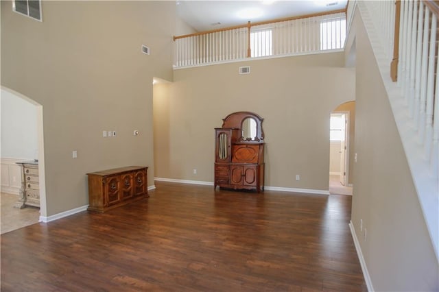 unfurnished living room with dark wood-style floors, arched walkways, and visible vents