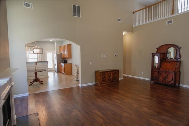 unfurnished living room with arched walkways, dark wood-style flooring, and visible vents