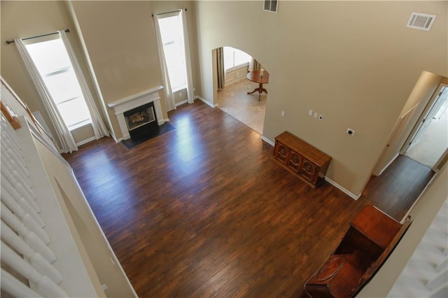 unfurnished living room with arched walkways, dark wood-style flooring, a fireplace with flush hearth, visible vents, and baseboards