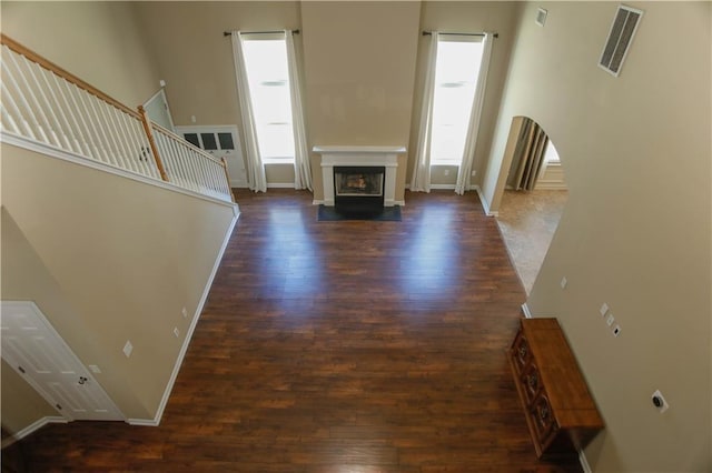 unfurnished living room featuring plenty of natural light, a fireplace, visible vents, and dark wood-type flooring