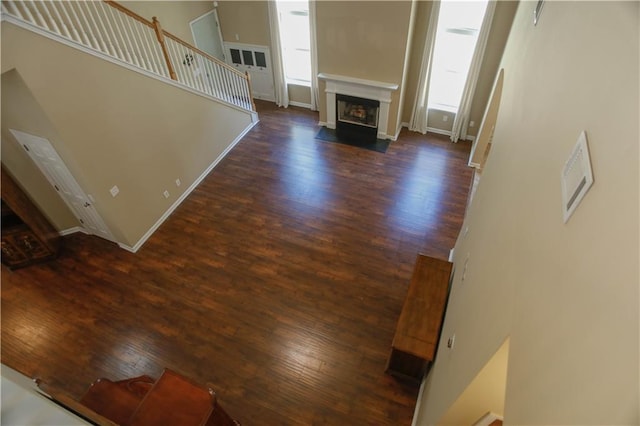 unfurnished living room featuring dark wood-style floors, stairway, a fireplace with flush hearth, and baseboards