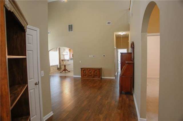 hallway with visible vents, a high ceiling, arched walkways, and dark wood-style flooring