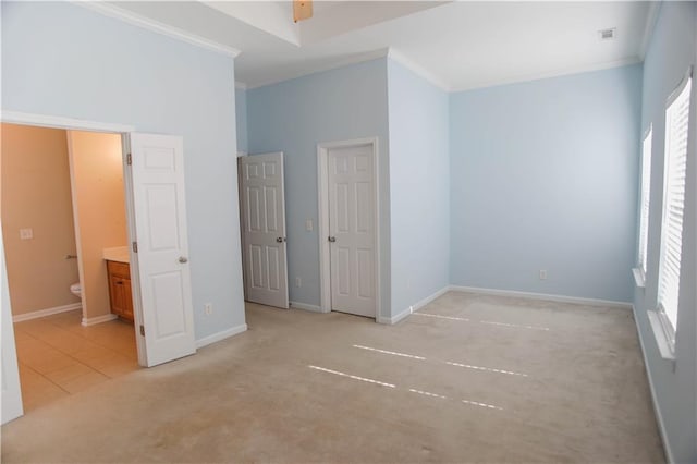 unfurnished bedroom featuring light carpet, multiple windows, baseboards, and crown molding