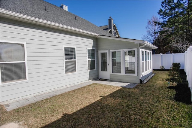 rear view of property featuring a shingled roof, a lawn, a chimney, and fence private yard