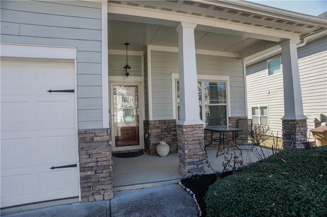 view of exterior entry featuring a garage, covered porch, and stone siding