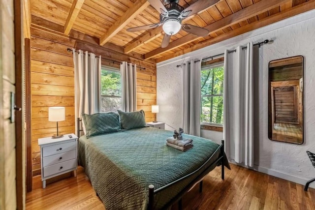 bedroom featuring ceiling fan, beam ceiling, hardwood / wood-style flooring, multiple windows, and wooden ceiling