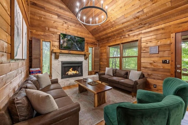 living room with a notable chandelier, wood walls, a stone fireplace, and wooden ceiling