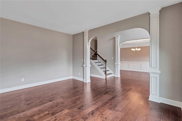 spare room featuring an inviting chandelier, decorative columns, and dark hardwood / wood-style floors