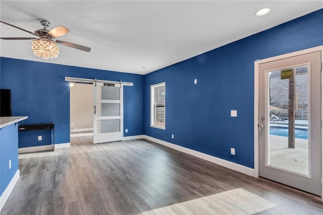 unfurnished living room featuring wood finished floors, baseboards, and a barn door