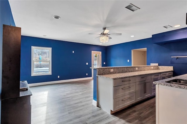 kitchen with light stone counters, ceiling fan, hardwood / wood-style floors, and a kitchen island