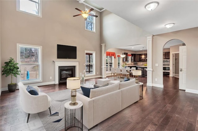 living room with a glass covered fireplace, dark wood-style flooring, a healthy amount of sunlight, and decorative columns