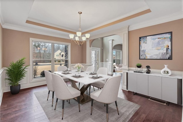 dining room with a tray ceiling, dark wood-style flooring, a decorative wall, and arched walkways