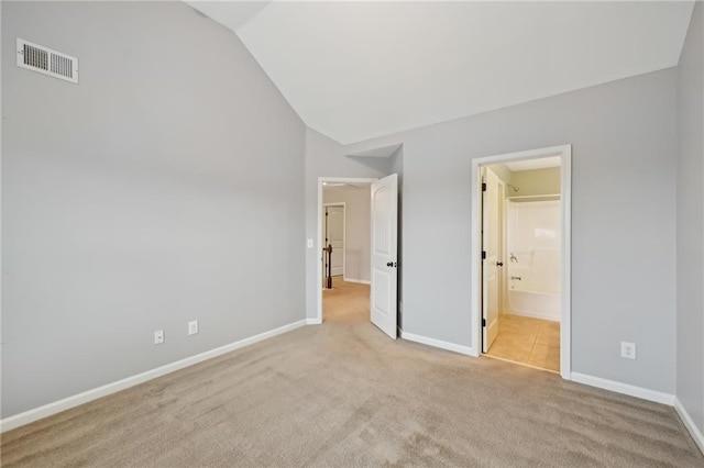 unfurnished bedroom with lofted ceiling, ensuite bathroom, and light carpet