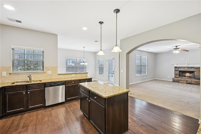 kitchen with pendant lighting, sink, dishwasher, a fireplace, and light stone countertops