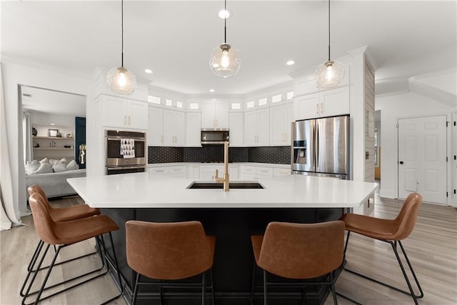 kitchen featuring a large island with sink, sink, light hardwood / wood-style flooring, decorative backsplash, and appliances with stainless steel finishes