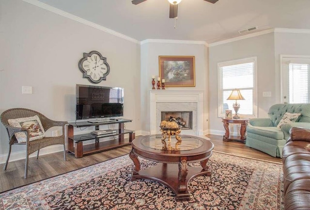 living room featuring crown molding, wood-type flooring, ceiling fan, and a high end fireplace