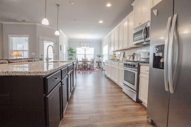 kitchen featuring appliances with stainless steel finishes, hanging light fixtures, sink, white cabinetry, and a kitchen island with sink