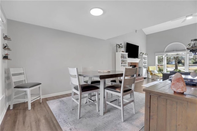 dining room with light hardwood / wood-style floors, a brick fireplace, and lofted ceiling