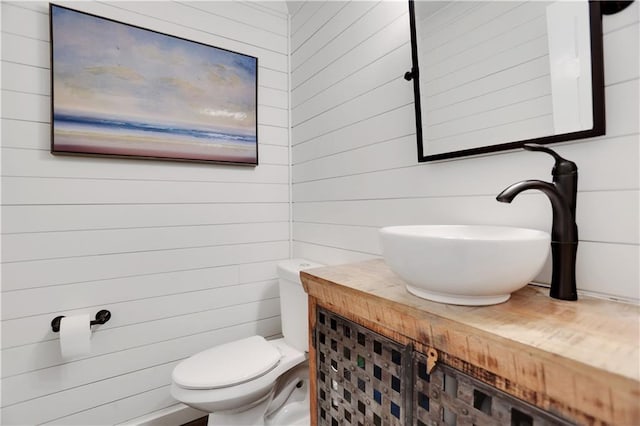 bathroom with toilet, wood walls, and vanity