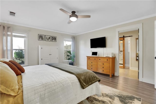 bedroom with hardwood / wood-style flooring, multiple windows, a barn door, ornamental molding, and ceiling fan