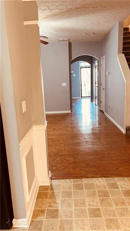 hall featuring visible vents, stairway, light wood-style floors, arched walkways, and a textured ceiling