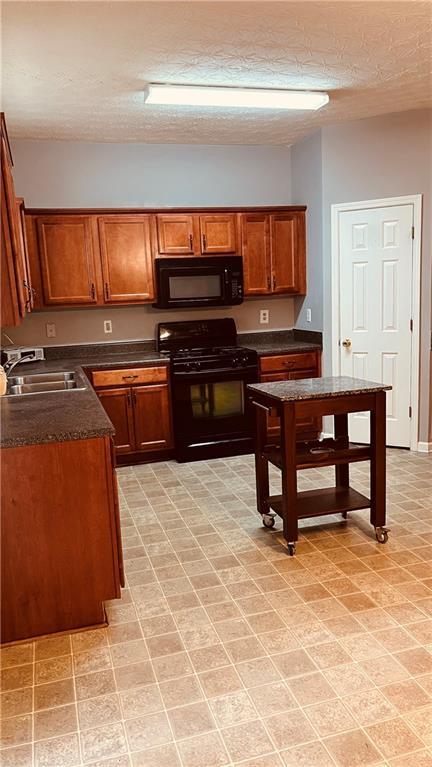 kitchen featuring brown cabinets, black appliances, a sink, dark countertops, and a textured ceiling