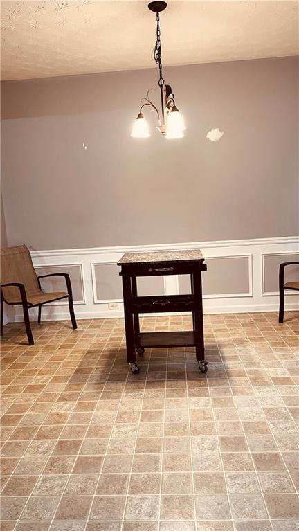 unfurnished dining area with a wainscoted wall, brick floor, a decorative wall, and an inviting chandelier