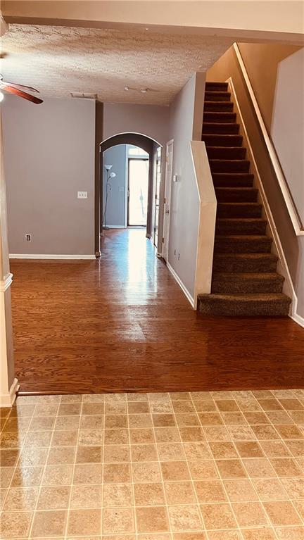 interior space featuring a ceiling fan, a textured ceiling, arched walkways, baseboards, and stairs