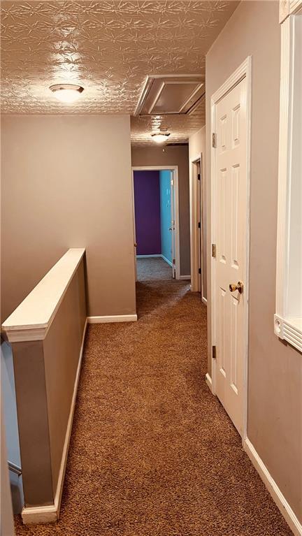 corridor featuring attic access, carpet, and baseboards