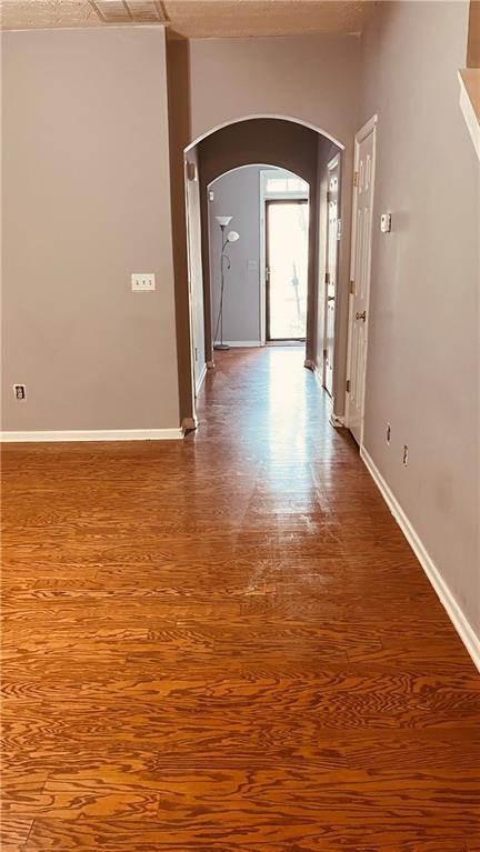 hall featuring wood finished floors, arched walkways, and baseboards