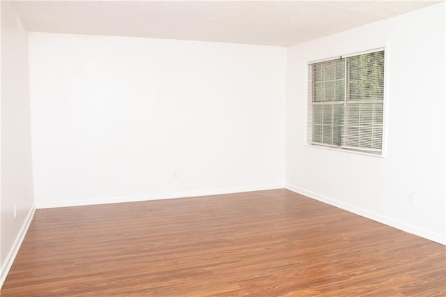 spare room with baseboards and wood finished floors