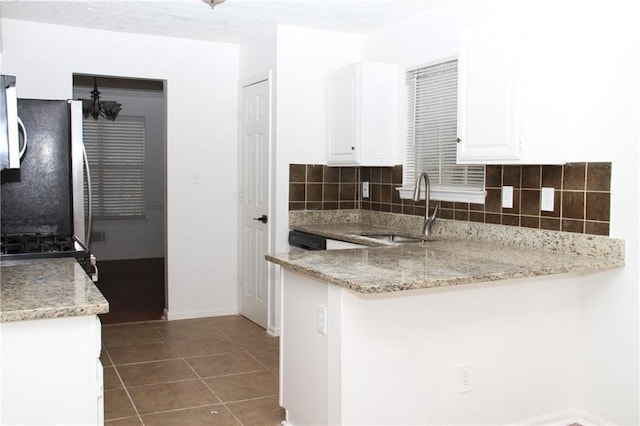 kitchen featuring decorative backsplash, a peninsula, dark tile patterned floors, white cabinetry, and a sink