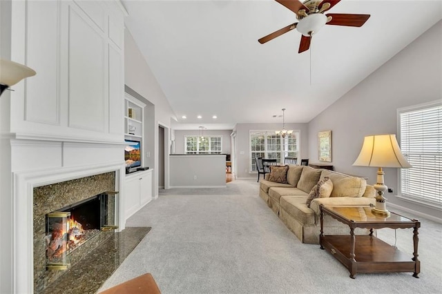 living room with baseboards, light colored carpet, vaulted ceiling, a fireplace, and ceiling fan with notable chandelier