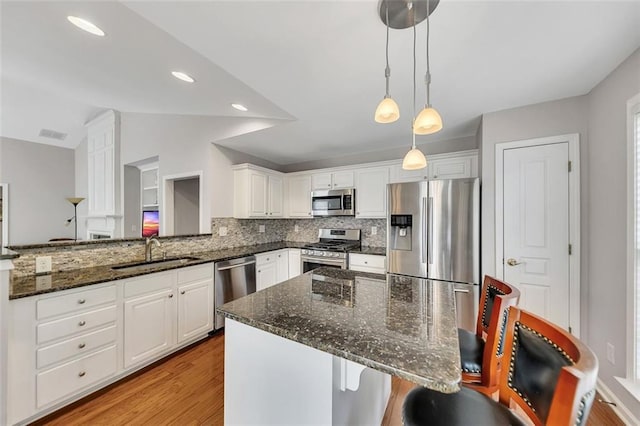 kitchen featuring lofted ceiling, a sink, appliances with stainless steel finishes, light wood-type flooring, and backsplash