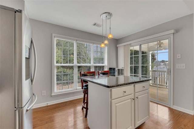 kitchen with hanging light fixtures, light wood-style floors, white cabinetry, a kitchen island, and stainless steel fridge