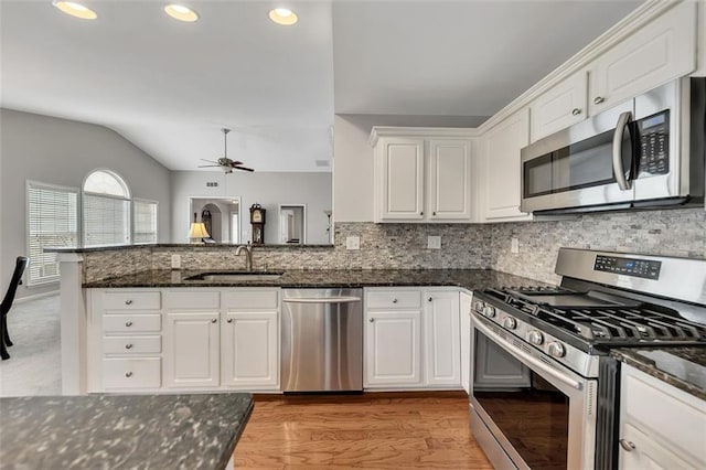 kitchen featuring lofted ceiling, appliances with stainless steel finishes, white cabinets, a sink, and a peninsula