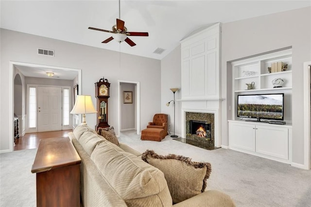 living area with lofted ceiling, a high end fireplace, visible vents, and light colored carpet