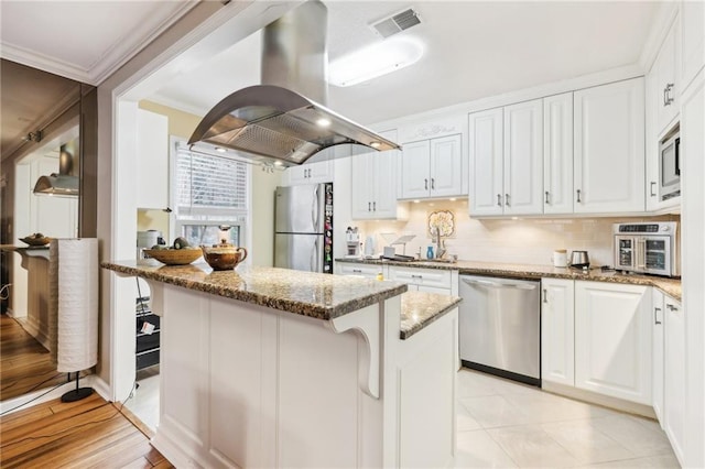 kitchen featuring light stone countertops, white cabinets, island range hood, a kitchen island, and appliances with stainless steel finishes