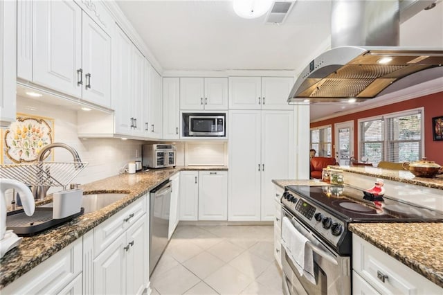 kitchen featuring white cabinetry, island exhaust hood, appliances with stainless steel finishes, and dark stone counters