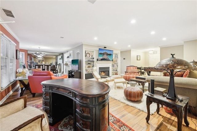 living room featuring built in shelves, light hardwood / wood-style floors, an inviting chandelier, and ornamental molding