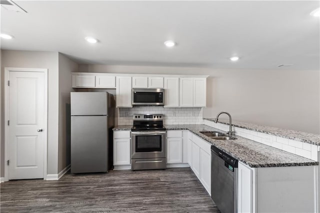 kitchen featuring a peninsula, a sink, dark stone counters, white cabinetry, and appliances with stainless steel finishes