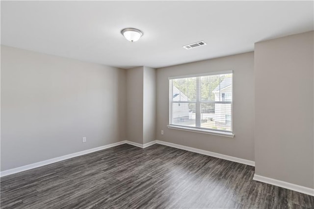 unfurnished room with baseboards, visible vents, and dark wood-style flooring