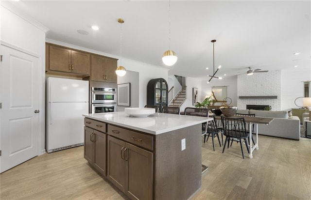 4317 Azalea Ridge Way, Hoschton, GA 30548 - kitchen with freestanding refrigerator, double oven, ceiling fan, a fireplace, and light wood finished floors