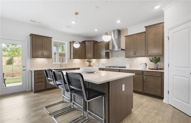 4317 Azalea Ridge Way, Hoschton, GA 30548 - kitchen featuring wall chimney range hood, a center island, light countertops, light wood-style floors, and ornamental molding