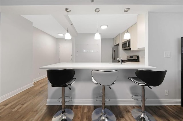 kitchen with a peninsula, wood finished floors, light countertops, appliances with stainless steel finishes, and a kitchen bar