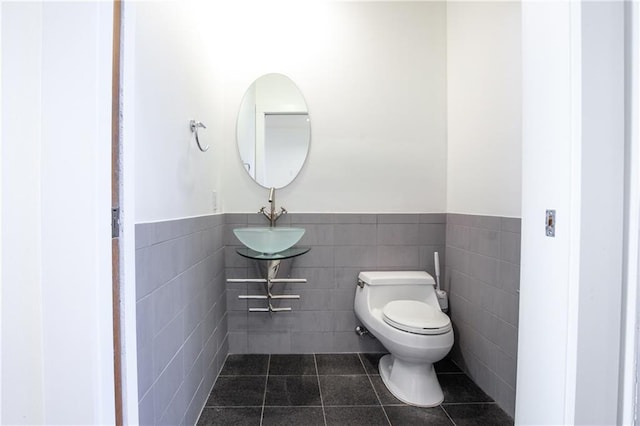 bathroom with toilet, sink, tile patterned floors, and tile walls