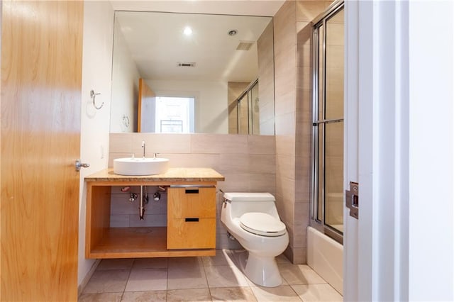 full bathroom with toilet, tile patterned flooring, vanity, tile walls, and combined bath / shower with glass door