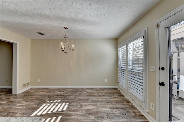 unfurnished dining area featuring hardwood / wood-style flooring, a textured ceiling, and an inviting chandelier