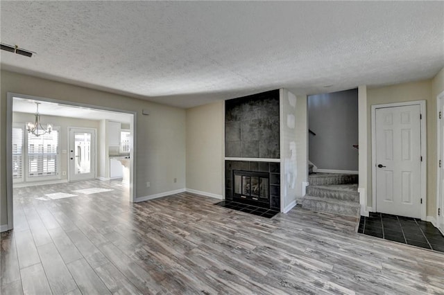 unfurnished living room with a textured ceiling, a notable chandelier, wood-type flooring, and a fireplace